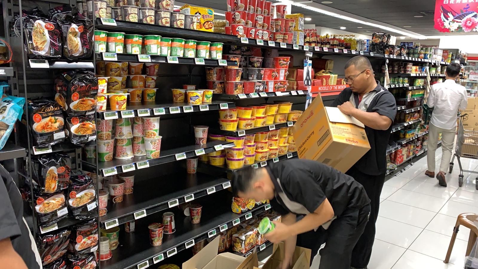 Supermarket staff restocking shelves with instant noodles.