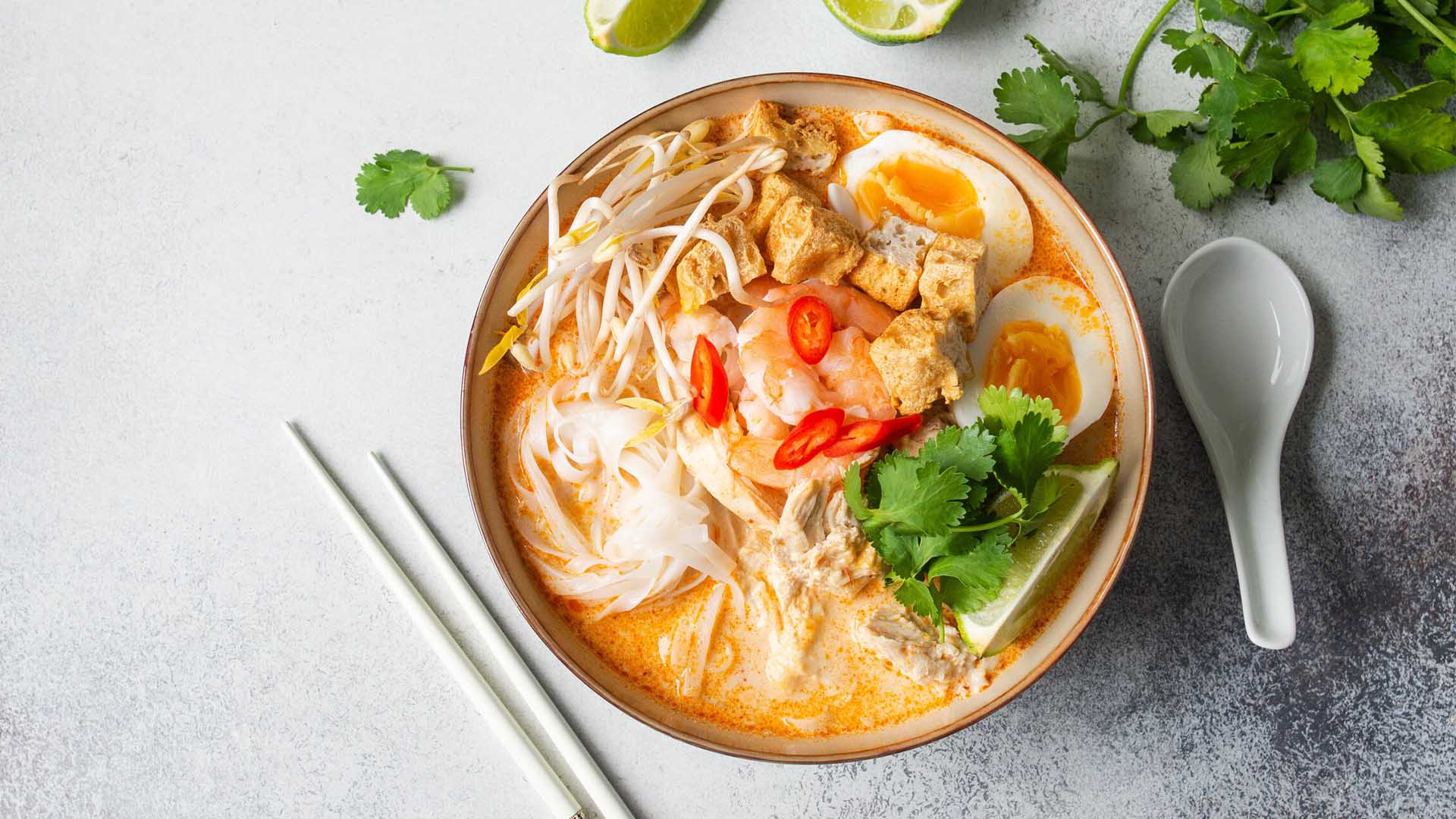 Laksa noodles soup with chicken, prawn and tofu in a bowl on grey surface
