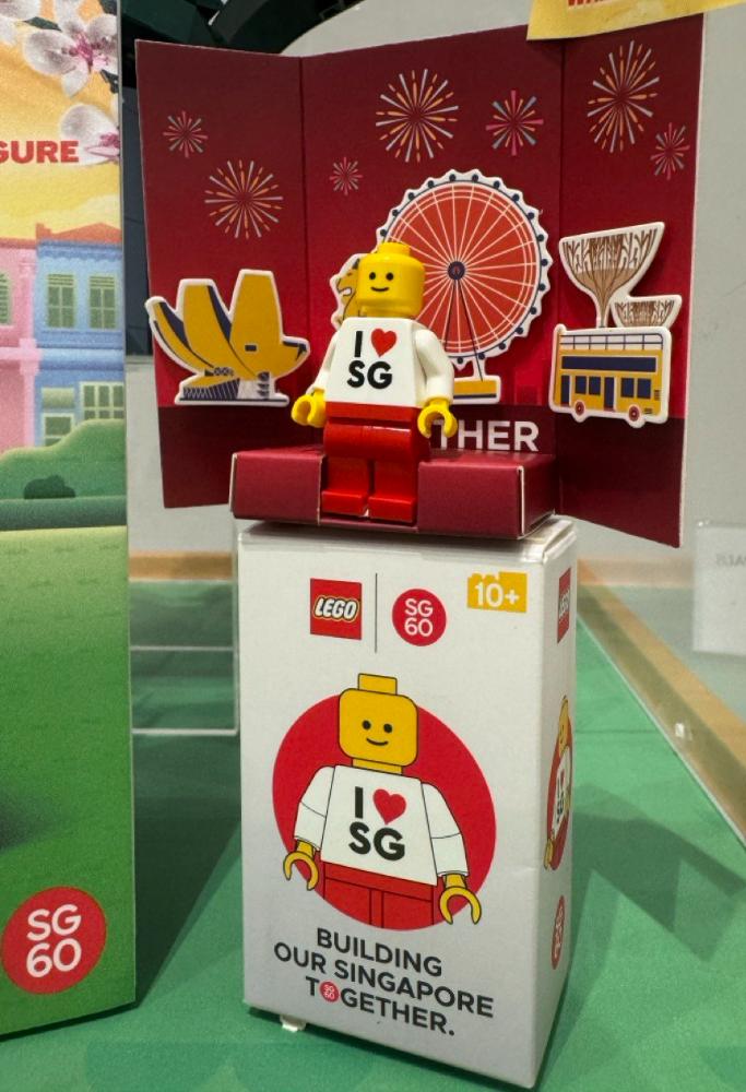Exclusive SG60 LEGO Singapore minifigure, a commemorative item released to celebrate Singapore's 60th anniversary in 2025. The minifigure features a classic LEGO smiley face and a white torso printed with 